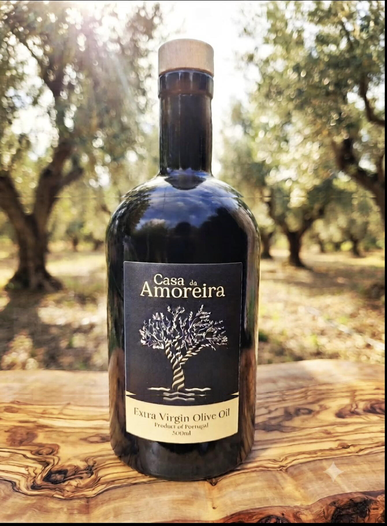 A bottle of Casa da Amoreira olive oil standing on an olive-wood board in the sunlit grove